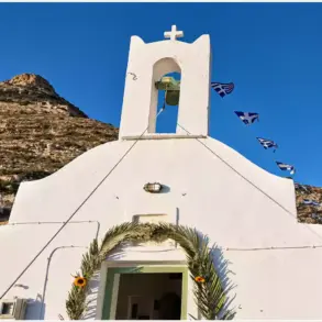Weiße Fassade der Kirche der heiligen Marina auf Sifnos mit Glockengiebel und einem mit Palmwedeln geschmückten Eingang.