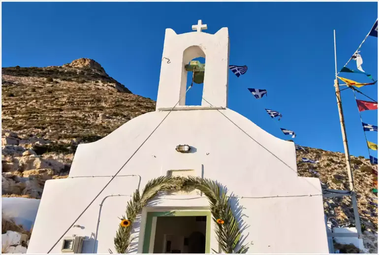Λευκή πρόσοψη του ναού της Αγίας Μαρίνας Σίφνου, με καμπαναριό και είσοδο στολισμένη με φοινικόφυλλα.