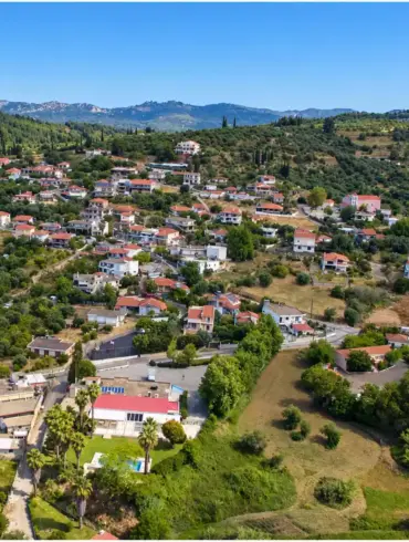 Agios Georgios de Pirgos visto desde un dron, con tejados de teja entre olivares y colinas bajas.