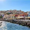 Case colorate di Parga sopra il lungomare, con gli ombrelloni dei locali e la scogliera che protegge la riva.