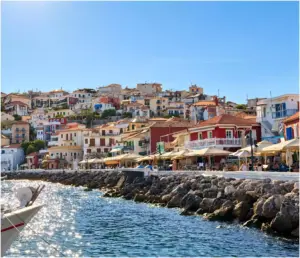Colourful houses of Parga rising above the waterfront, with café umbrellas and the rock armour lining the shore.