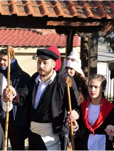 კეპიანი, თეთრსარტყლიანი მამაკაცები კომბლებით, მხრებზე წითელი თავსაფრებითა და თეთრი წინსაფრებით მორთული ახალგაზრდა მოცეკვავე ქალების გვერდით.